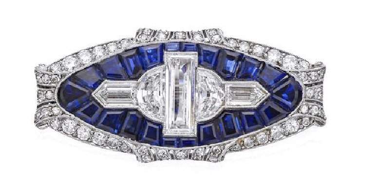 An Art Deco sapphire and diamond brooch, 1930s Of oval form, set to the centre with a geometric formation of baguette, half-moon shaped and bullet-shaped diamonds, all within a surround of calibré-cut sapphires and a pierced millegrain-set border of old round brilliant and single-cut diamonds with scroll detail, length 38mm, the diamonds estimated to weigh approximately 3.10cts in total